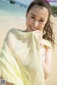 A woman in a bikini holding a yellow scarf on the beach.
